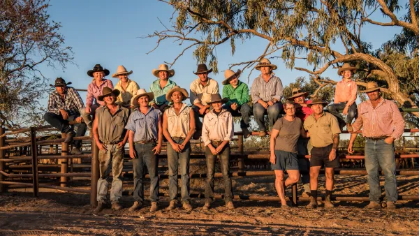 Group of males and females wearing cowboy hats in front of country fence